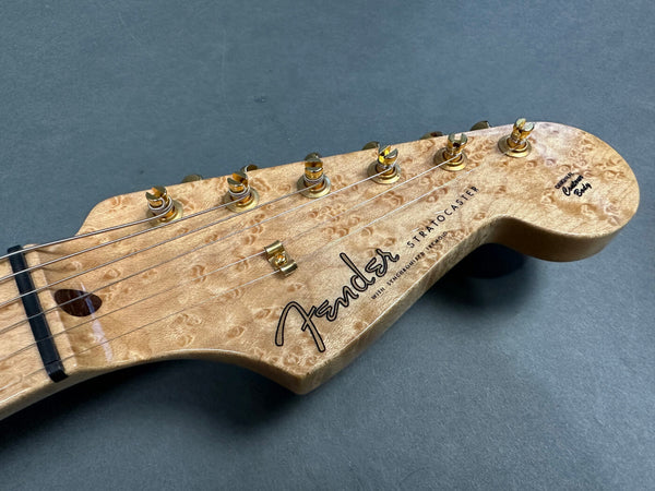 Close-up of Fender Stratocaster guitar headstock with figured maple wood and gold tuning pegs on gray background