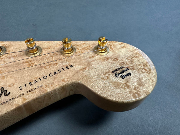Close-up of a natural wood grain Fender Stratocaster guitar headstock with gold tuning pegs and "Original Contour Body" text on the side