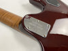 Close-up of Ernie Ball Music Man guitar neck plate on a polished dark red guitar body with flamed maple neck.
