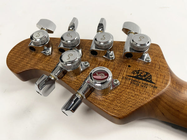 Close-up of guitar headstock with chrome tuning pegs and California Heritage logo on natural wood grain finish