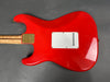 Back of red electric guitar body with white plastic backplate and natural wood neck with gold neck plate on gray background