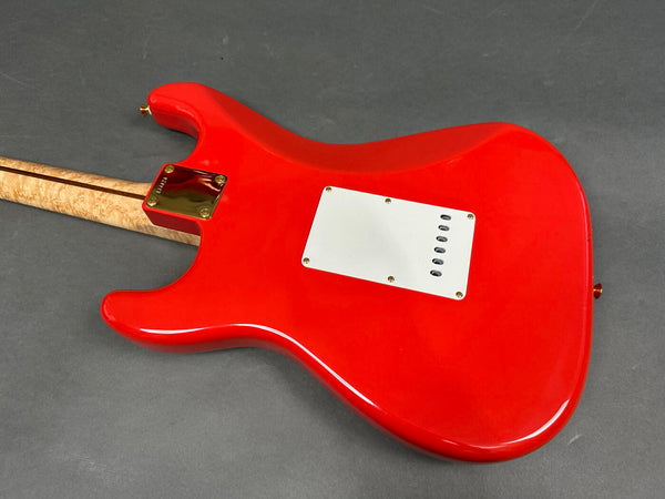 Back view of red electric guitar with white tremolo cavity cover and natural wood neck with stripe on dark gray background