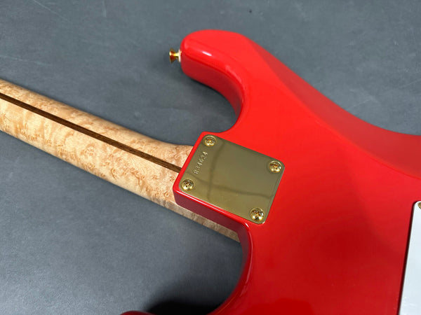 Close-up of electric guitar neck joint with figured maple neck and vibrant red body featuring gold neck plate with serial number on grey background