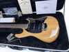 Natural wood finish electric guitar with black pickguard and three single-coil pickups in hard case with certificate of authenticity and Ernie Ball accessories