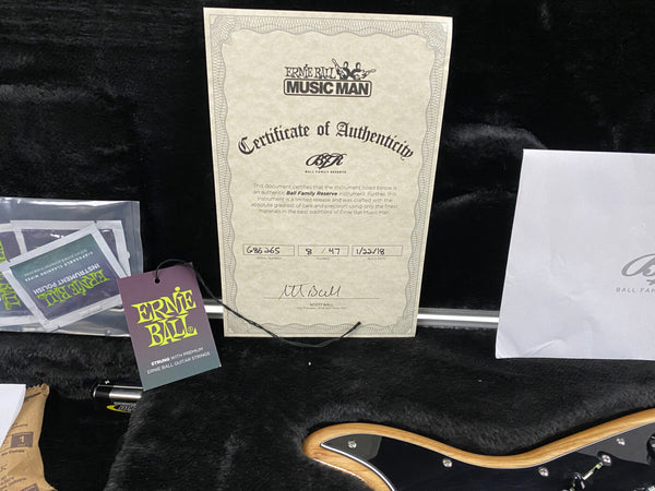 Ernie Ball Music Man Certificate of Authenticity for Ball Family Reserve guitar with serial number 686265 and signed by Scott Ball, displayed inside a guitar case with Ernie Ball guitar string packaging and part of a natural wood guitar body visible.