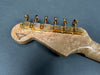 Close-up of guitar headstock with birdseye maple wood finish and gold tuning pegs on gray background