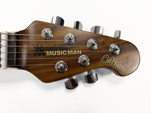Close-up of Music Man Cutlass guitar headstock with chrome tuning pegs and wooden finish against white background