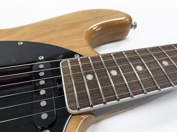 Close-up of electric guitar fretboard and black pickup on natural wood body with chrome frets and white dot inlays