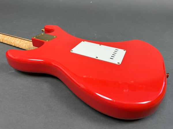 Back view of bright red electric guitar with white backplate and curly maple neck on gray surface