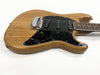 Electric guitar with natural wood finish and black pickguard featuring three single-coil pickups, volume and tone knobs, and chrome bridge on white background.