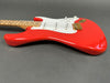 Close-up of red electric guitar body with white pickguard, three single-coil pickups, gold bridge, and maple neck with bird inlays on fretboard.