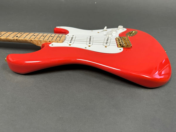 Close-up of red electric guitar body with white pickguard, three single-coil pickups, gold bridge, and maple neck with bird inlays on fretboard.