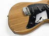 Close-up of natural wood electric guitar body with black pickguard, three single-coil pickups, volume and tone control knobs, and chrome bridge on white background