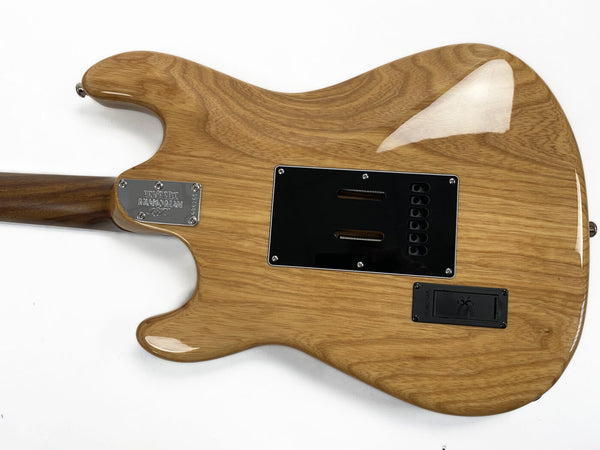 Back view of natural wood finish Ernie Ball Music Man electric guitar body with black plastic cover plates and chrome neck plate on white background