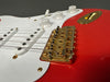 Close-up of red electric guitar with white pickguard, gold Fender bridge, volume and tone knobs, and six strings