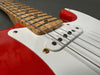 Close-up of red electric guitar body with white pickguard, single-coil pickups, maple neck, and metal strings