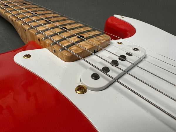 Close-up of red electric guitar body with white pickguard, single-coil pickups, maple neck, and metal strings