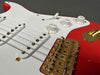 Close-up of red and white electric guitar body showing white volume and tone control knobs, white pickups, and gold bridge with Fender engraving