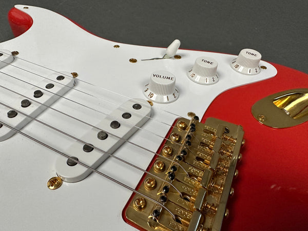 Close-up of red and white electric guitar body showing white volume and tone control knobs, white pickups, and gold bridge with Fender engraving