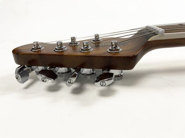 Close-up of brown guitar headstock with chrome tuning pegs and strings on white background