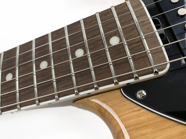 Close-up view of electric guitar rosewood fretboard with metal frets, white dot inlays, steel strings, and natural wood body finish near black pickguard and pickup screws