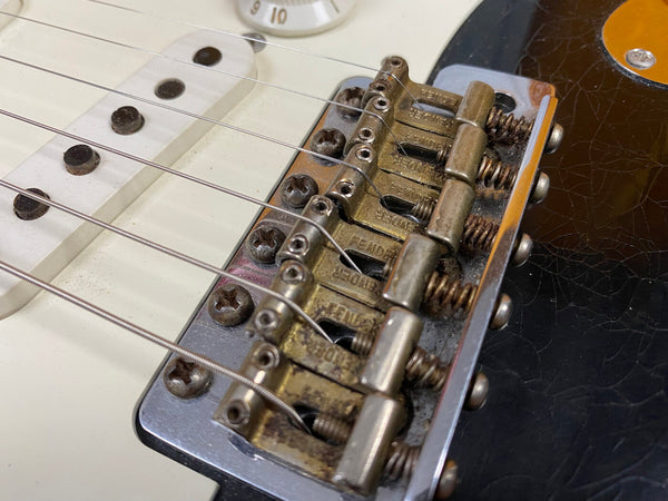 Close-up of vintage electric guitar bridge and white single-coil pickup with six strings and rusty screws on black and white guitar body
