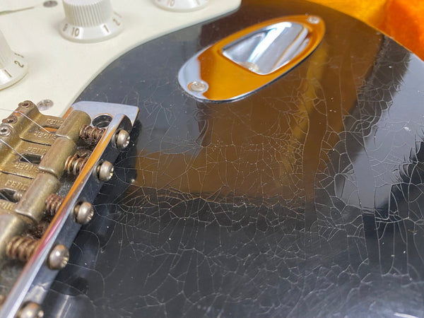 Close-up of black electric guitar body with crackle finish near bridge and control knobs, showing vintage wear and rusty screws