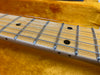 Close-up of maple guitar neck with metal frets and black dot position markers on light wood fretboard against orange fabric background