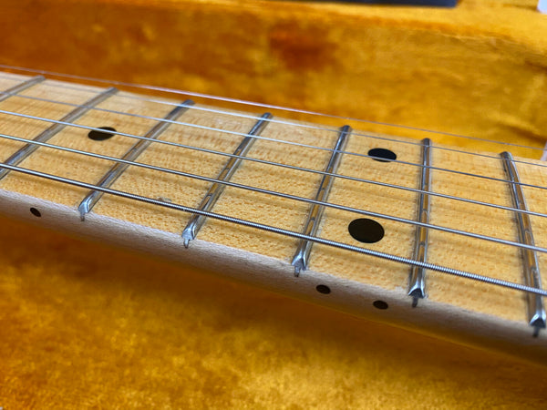 Close-up of maple guitar neck with metal frets and black dot position markers on light wood fretboard against orange fabric background