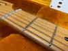 Close-up of maple guitar neck with detailed wood grain and metal frets, electric guitar strings, and a section of the orange velvet-lined guitar case interior.