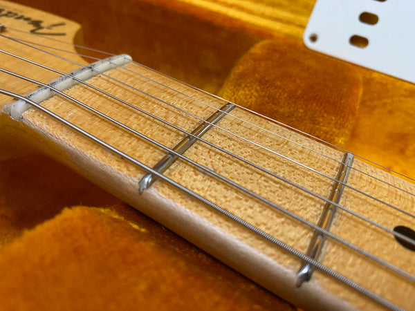 Close-up of maple guitar neck with detailed wood grain and metal frets, electric guitar strings, and a section of the orange velvet-lined guitar case interior.