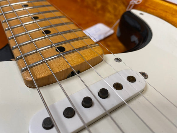 Close-up of electric guitar maple fretboard with metal frets and steel strings over white single-coil pickups on cream body