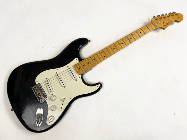 Fender Stratocaster electric guitar with black body and maple neck, three single-coil pickups, white pickguard, and vintage-style tremolo bridge, laid flat on white background.