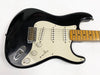 Black electric guitar with white pickguard, three single-coil pickups, maple neck, and vintage-style tremolo bridge on white background