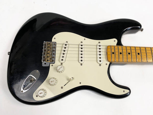 Black electric guitar with white pickguard, three single-coil pickups, maple neck, and vintage-style tremolo bridge on white background