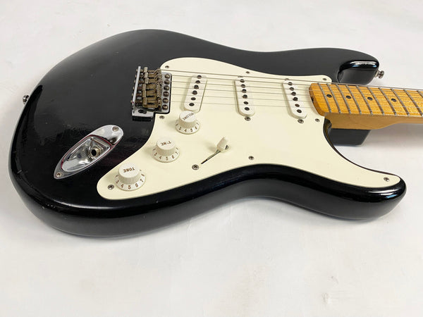 Black electric guitar with white pickguard and maple fretboard, vintage style Stratocaster design with three single-coil pickups and tone and volume control knobs