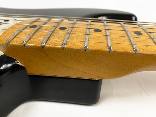 Close-up of maple guitar fretboard with dot inlays and steel frets on electric guitar neck resting on black guitar stand