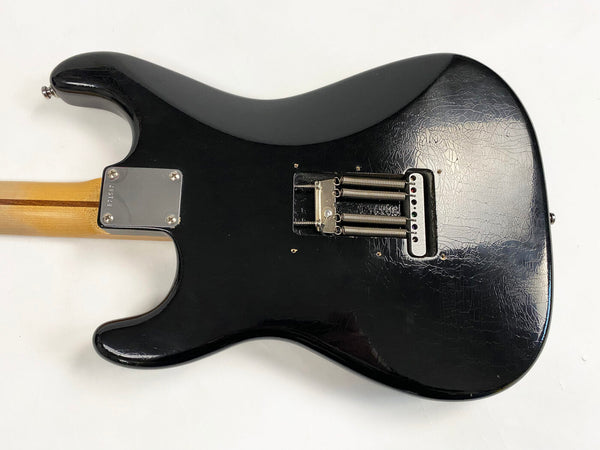 Black electric guitar body back with vintage-style tremolo springs and natural wood neck with four-bolt neck plate on white background