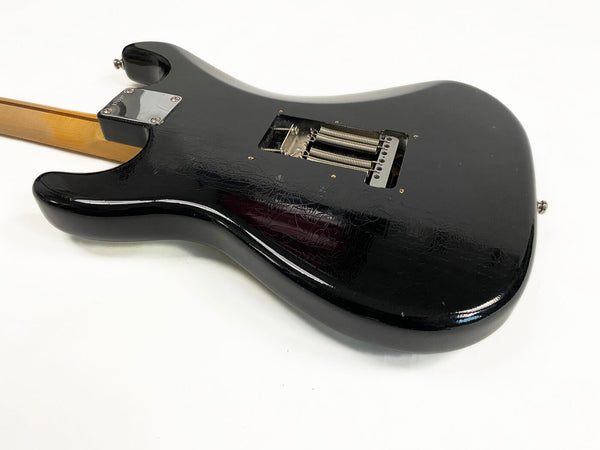Black electric guitar body with visible tremolo springs and wooden neck on white background, vintage crackled finish