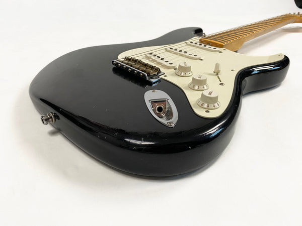 Close-up of black electric guitar body with white pickguard, three single-coil pickups, and control knobs on a white background.