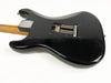 Black electric guitar body with visible tremolo springs and natural wood neck on white background, showing wear and finish checking.