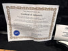 Certificate of Authenticity from G&L Musical Products Inc. for guitar serial number 21076, detailing the company's history and Leo Fender's legacy, placed on black fabric background next to guitar warranty registration card and part of a black and white guitar body.