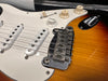 Close-up of sunburst electric guitar body showing white pickguard, three single-coil pickups, chrome bridge, and volume and tone control knobs