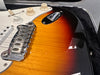 Close-up of sunburst electric guitar body showing chrome bridge, volume and tone control knobs, and pickup selector switch in guitar case