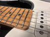 Close-up view of electric guitar maple fretboard with metal frets, black dot inlays, and white single-coil pickups, showcasing guitar strings and part of the black and white guitar body