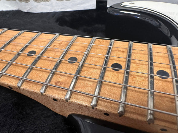 Close-up of maple guitar neck and fretboard with dot inlays and metal frets on black electric guitar body