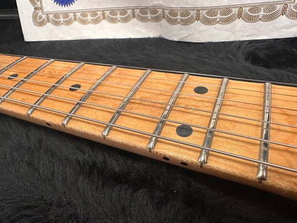 Close-up of maple guitar neck and fretboard with dot inlays and metal frets on black plush background