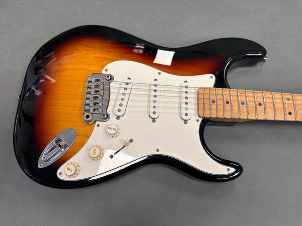 Sunburst electric guitar with white pickguard and maple fretboard on gray background