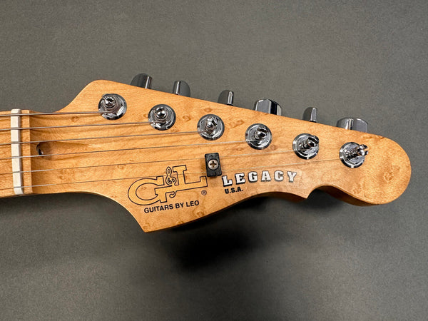 Close-up of G&L Legacy electric guitar headstock with tuning pegs and natural wood finish against gray background