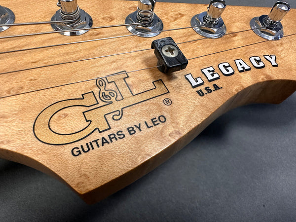 Close-up of natural wood GT Legacy USA electric guitar headstock with tuning pegs and string tree, showcasing Guitars by Leo logo and detailed wood grain.